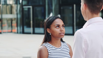 Close-up of mixed-race girl quarreling with her boyfriend outdoors and then leaving him alone. Couple quarrel at a date.