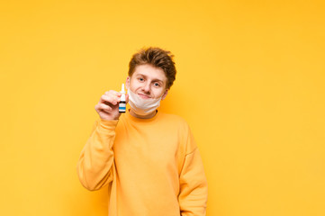 A funny guy with a removed mask stands on a yellow background, looks at the camera with a smile on his face and shows nasal spray to the camera. Fighting the undead in a pandemic. COVID-19. Quarantine