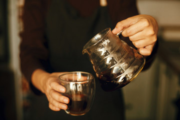 Person pouring fresh aromatic coffee from glass kettle in cup. Alternative coffee brewing, v60. Professional barista in black uniform making drip coffee