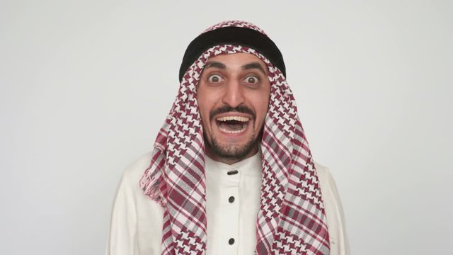 A funny cheerful Arab looks at the camera and laughs loudly. An Arab with stubble and a mustache, in kandura, smiles broadly and looks at the camera
