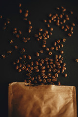Coffee beans scattered from paper pack on black background Flat lay. Fresh aromatic roasted coffee beans top view. Coffee shop concept.  Dark moody image