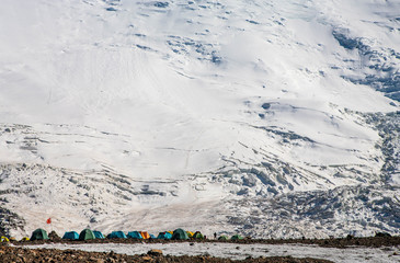 Tent camp at the foot of the snowy slope of mountain. Expedition. Hiking in the mountains.