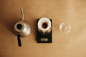 Drip coffee flat lay. Steel kettle, glass flask with filter pour over on scale and glass cup on brown background. Brewing aromatic fresh  alternative coffee,  v60