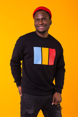 Youth street fashion concept - Portrait of confident sexy black man in stylish sweatshirt on yellow background.