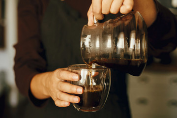 Professional barista in black uniform making drip coffee. Person pouring fresh aromatic coffee from glass kettle in cup. Alternative coffee brewing, v60.