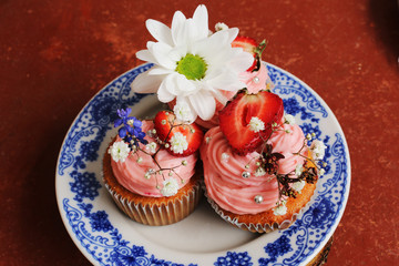 Homemade cream cupcakes decorated with fresh flowers and strawberries. Ready desserts at home!