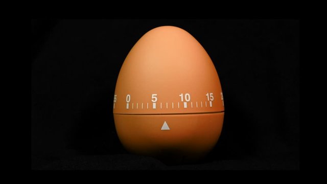 Zoom in close up to a color changing egg shaped kitchen timer.  Time lapse of a kitchen egg shaped cooking time countdown timer.