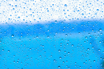 blue rain water drops on a window glass close up , colored drop background macro in a blue light