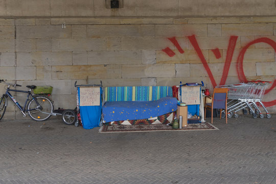 Schlafplatz mit in Einkaufswägen zusammengetragenem Hab und Gut eines Obdachlosen auf der Strasse unter einer Brücke