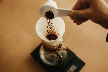 Hands pouring grounded coffee in filter. Preparing for alternative coffee brewing v60. Person...