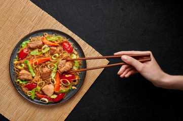 Pad Woon Sen or Thai Pork Glass Noodle Stir-Fry in black plate on dark slate backdrop. Pad Woon Sen is a Thai cuisine dish of glass bean noodles, meat, tomatoes, carrots, egg, sauces. Thai Food.