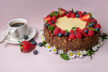 Cheesecake decorated with berries and flowers on a light pink background with a cup of coffee on the left side.