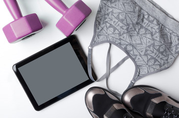 Top view of grey top for sport, tablet pc, sneakers, dumbbells on the white background.Concept of online workout at home