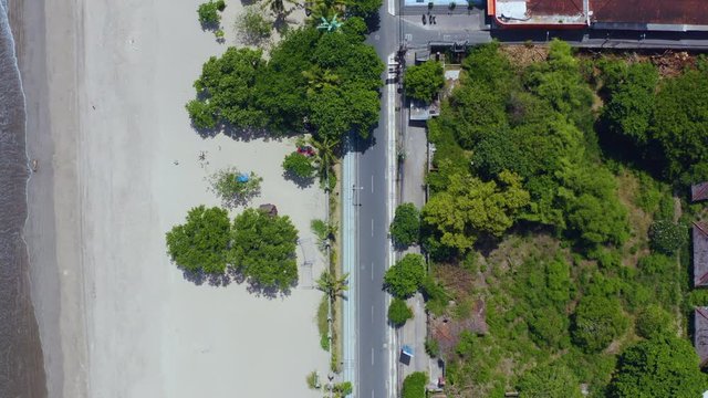 Overhead view along the largely empty and deserted Jalan Pantai Kuta Road and beaches of Kuta in Bali, Indonesia. Aerial drone overhead slow forward motion