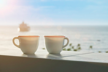Two cups of coffee on a balcony with a view to the ocean. Sunny beautiful morning. Sea and ship in...