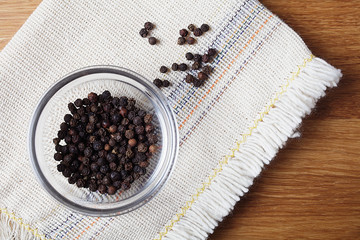 Fototapeta na wymiar black pepper peas in a glass bowl on a linen napkin, wooden table
