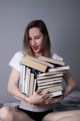 happy beautiful slim girl holds a lot of different books in her hands. Homeschooling. Studying in quarantine. Reading is helpful - vertical photo