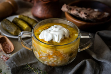 Hot soup with ribs and vegetables in a transparent plate close-up on a gray background. Pickle with sour cream