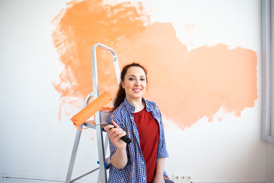 Renovation, redecoration and repair concept - Cheerful woman painting wall in new home.