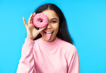 Attractive black woman having fun with donuts on blue background