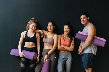 Happy smiling man and women looking at camera altogether in gym. Group of young people relaxing in gym after workout training with black background.