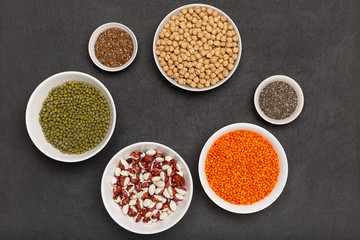Veggie protein sources on dark background, hlentils, chickpea, mung bean, bean, flax seed, chia on plates, copy space, top view