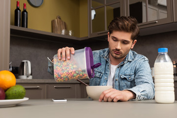 Selective focus of man pouring cereals in bowl near bottle of milk and fruits on kitchen table