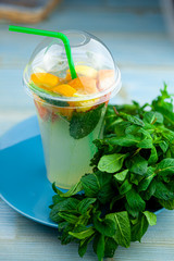 Mojito and Lemonade summer cold drink in a plastic glass with a straw. Coctail with mint, lemon, lime and ice. Serve at the bar. Beverage closeup.