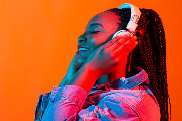 Neon portrait of young african woman listening music with earphones. - obrazy, fototapety, plakaty
