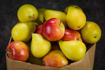 apples and pears in a paper bag of craft paper on a dark background