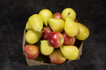 apples and pears in a paper bag of craft paper on a dark background