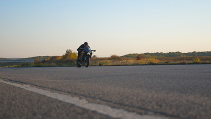 Obraz premium Young man racing fast his sport motorbike through empty highway. Motorcyclist riding on high speed along country asphalt road. Guy enjoying speed. Low angle view Slow motion