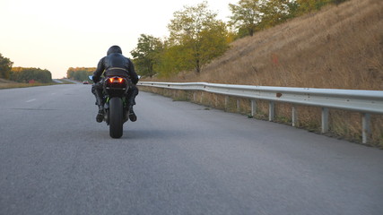 Unrecognizable man riding on modern sport motorbike at autumn highway. Motorcyclist racing his...