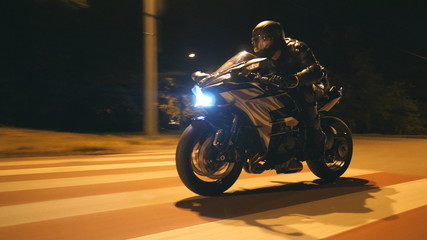 Young man in helmet riding fast on modern black sport motorbike at evening city street....