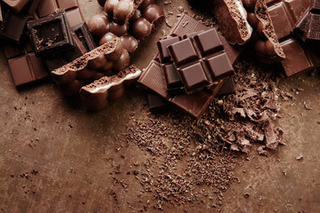 Composition of bars and pieces of different milk and dark chocolate, grated cocoa on a brown background top view close up