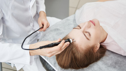 Beautician man doing anti-aging procedure of rf lifting face skin of a young woman in a white beauty parlor