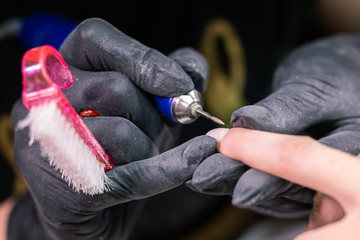 Hardware manicure in a beauty salon. Female manicurist is applying electric nail file drill to manicure on female fingers. Mechanical manicure close-up. Concept body care.