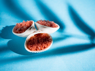 Orange bath salt with shells on a blue background with a shadow from a tropical plant. Copyspace,...