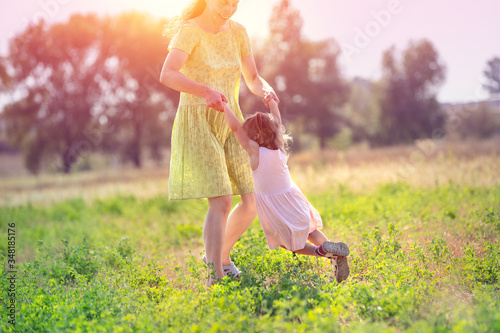Happy mother walking with little daughter outdoors in summer. The mother and kid run in the field. Happy childhood (family) and Mother's Day concept