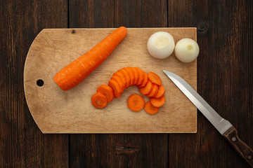 chopped carrots and onions on a wooden cutting board with a knife on a dark wooden table