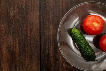 tomatoes and cucumber with drops of water on a dark wooden background on a plate top view