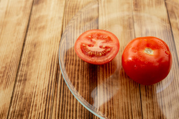 Whole tomato and half-sliced tomato on a wooden background with drops of water