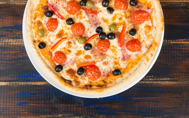 Fresh pizza with tomato sauce, black olives, mozzarella cheese, ham on wooden table closeup