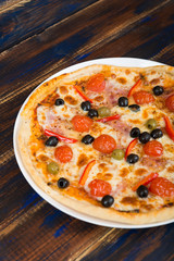 Fresh pizza with tomato sauce, black olives, mozzarella cheese, ham on wooden table closeup