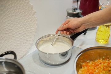 Bechamel sauce on an induction stove cook stirs with a spoon. We stay at home and cook lasagna in the kitchen.