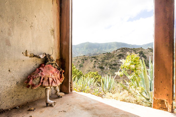 dirty faceless doll standing in an abandoned house in the mountains of La Gomera, Canary islands. Cursed, broken and evil girl mannequin in a red worn and damaged dress. Scary, haunted and lost place - obrazy, fototapety, plakaty