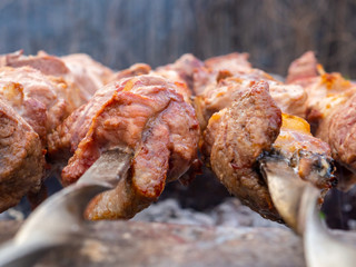Juicy and fresh slices of pork meat are strung on skewers and grilled in charcoal grill. Fragrant smoke. Natural meat dish outdoors on a spring day.