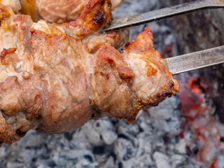 Juicy and fresh slices of pork meat are strung on skewers and grilled in charcoal grill. Fragrant smoke. Natural meat dish outdoors on a spring day.