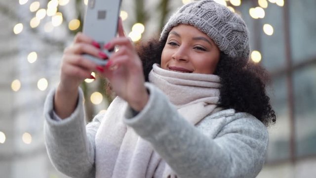 woman taking selfie on mobile phone outside on winter street spbi. concept new year, christmas holidays. mixed race hipster mixed race female taking picture on smartphone.