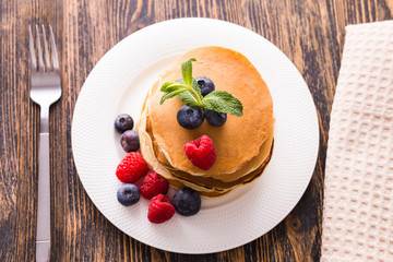 Homemade sweet pancakes with blueberries and raspberries on a white plate, top view.